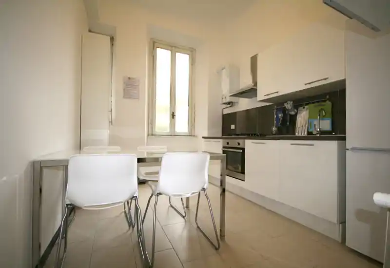 Cocina moderna y luminosa con muebles blancos, horno empotrado y una pequeña mesa con cuatro sillas — espacio compacto y funcional ideal para alquiler.