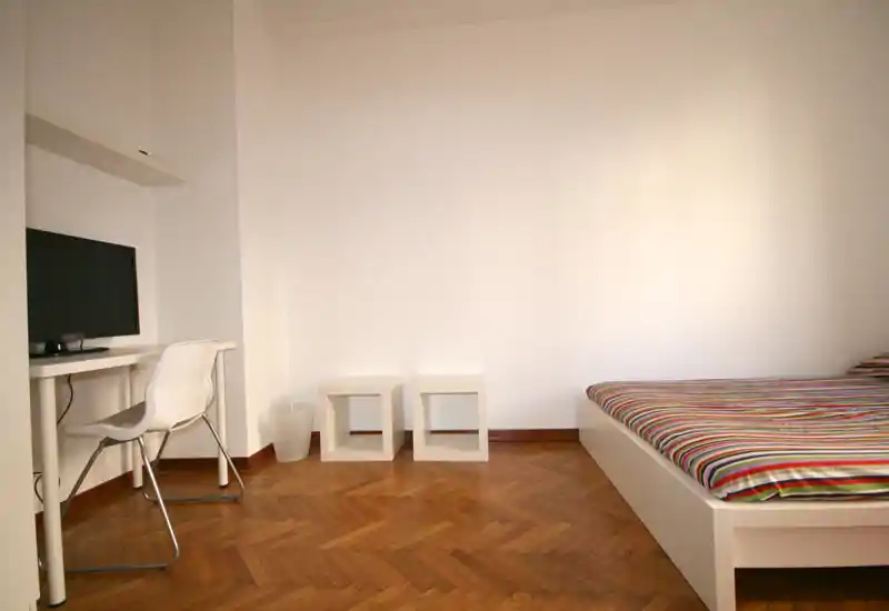 Dormitorio luminoso y minimalista con cama plataforma blanca y ropa de cama a rayas, suelo de parquet y pequeño escritorio—limpio, moderno y bien iluminado.
