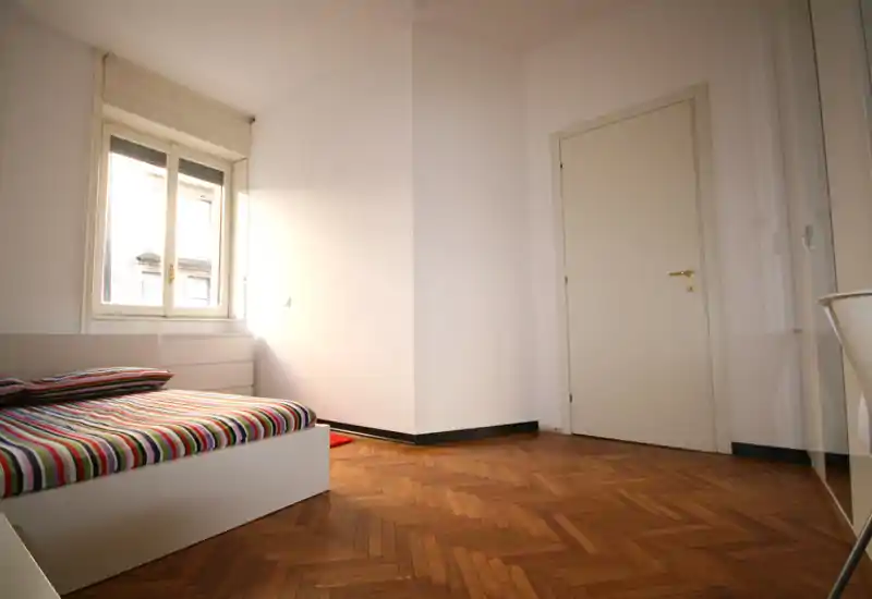 Dormitorio luminoso y minimalista con cama a rayas, gran ventana y suelo de parquet en espiga — espacio limpio y aireado, listo para mostrar.
