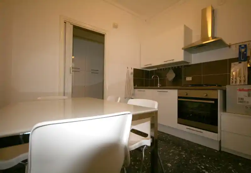 Cocina moderna y luminosa con horno integrado, campana de acero y mesa blanca con sillas — ideal para comidas informales en espacios compactos.