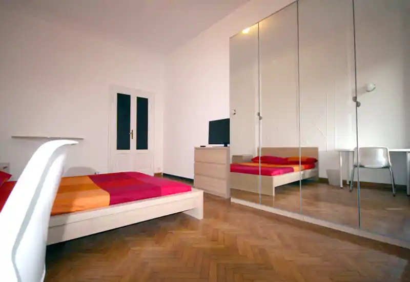 Camera da letto moderna e luminosa con letto basso, biancheria colorata e un grande armadio con ante a specchio che amplia lo spazio visivo.