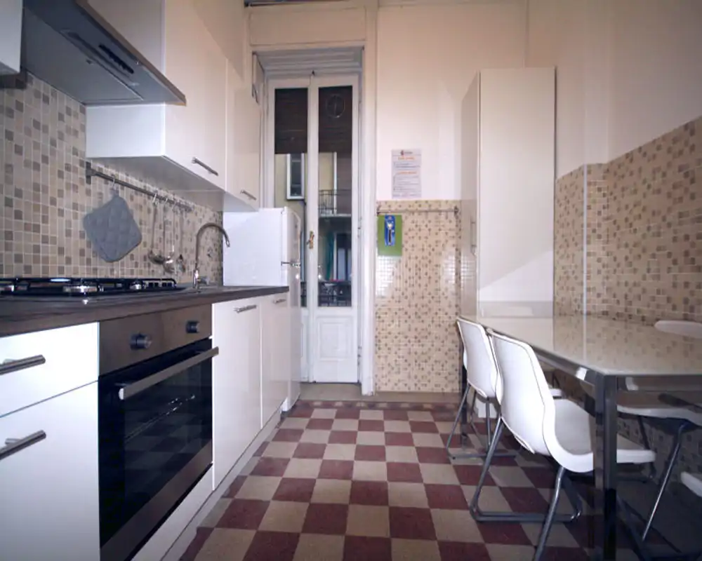 Cucina moderna a corridoio con pensili bianchi, forno incassato, microonde, paraschizzi piastrellato e un piccolo tavolo con sedie — ambiente luminoso e pulito, adatto alla preparazione dei pasti.