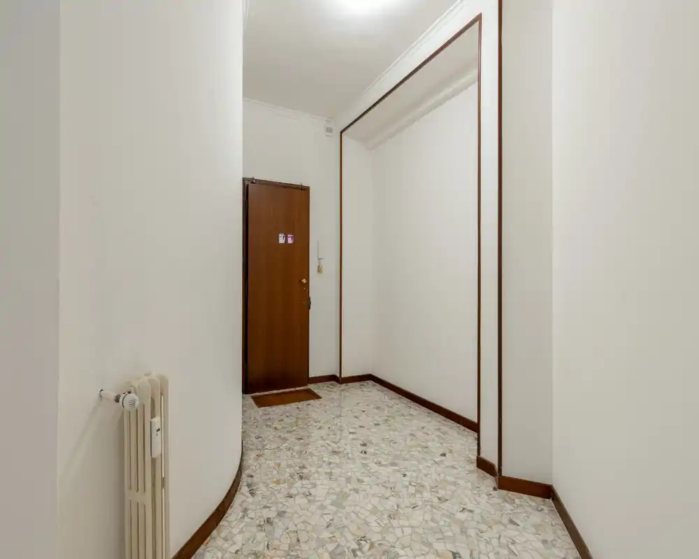 Bright, simple entrance hallway with a wooden main door, terrazzo flooring and neutral white walls — practical and well-lit.