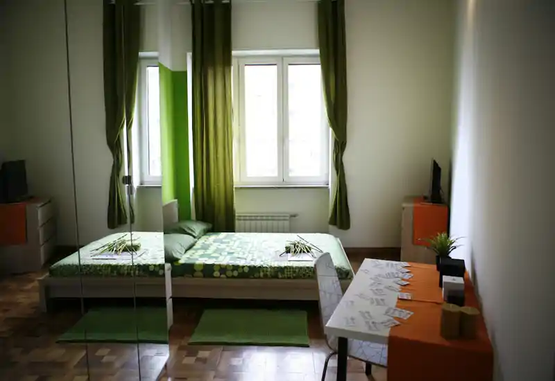 Dormitorio moderno y luminoso en tonos verdes: cama doble con ropa de cama estampada, alfombras y cortinas a juego, escritorio y armario con espejo que aportan profundidad y luz.