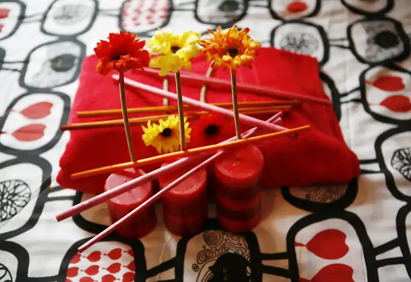 Plano cercano de la superficie de una cama decorada con textiles rojos, velas y flores, creando un ambiente cálido y acogedor—ideal para mostrar el estilo de la habitación y la ropa de cama.