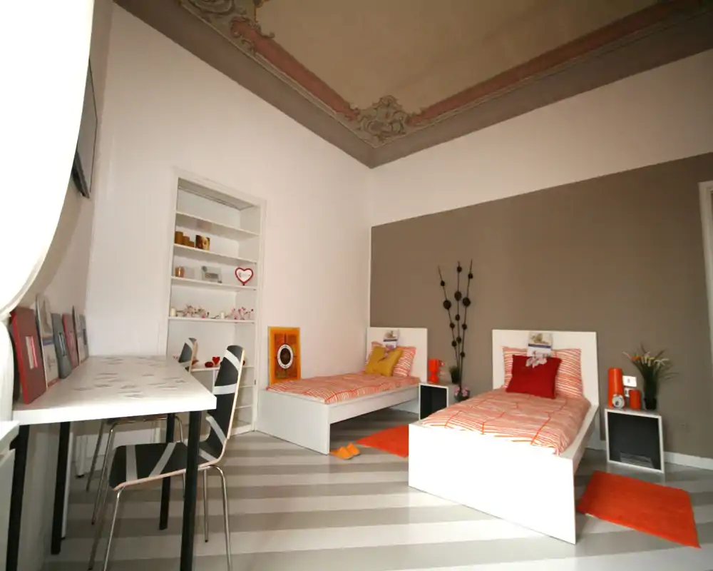 Bright, modern twin bedroom with two single beds, coordinated orange accents and a decorative painted ceiling; ideal for shared stays or children.