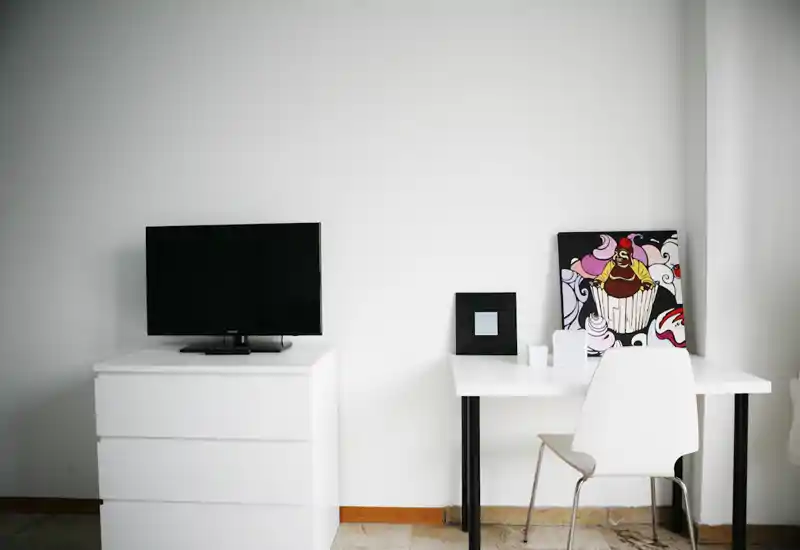 Minimal, modern living corner with a small TV on a white chest and a compact white desk with chair and artwork — bright, tidy and functional for a studio or small apartment.