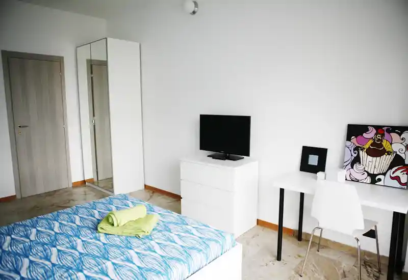 Bright, modern bedroom with a patterned blue bedspread, white storage drawers and a small desk — clean minimalist styling ideal for short-term stays.