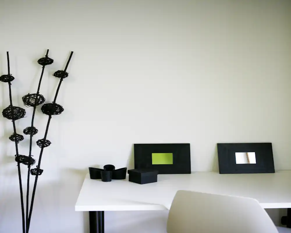 Angolo workspace minimalista con scrivania bianca, cornici e accessori neri decorativi e una sedia chiara — stile semplice e pulito adatto a un ufficio domestico o a un'area living rilassata.