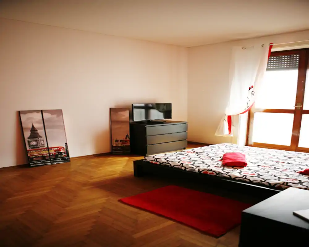 Chambre spacieuse et épurée avec lit bas sur plateforme, literie à motifs et lumière naturelle provenant d'une grande fenêtre — idéale pour une location moderne.
