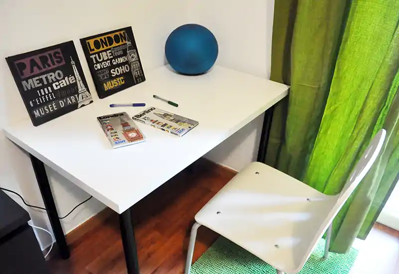 Rincón compacto y luminoso con escritorio blanco y silla junto a una cortina verde: ideal como espacio de trabajo o rincón de lectura.