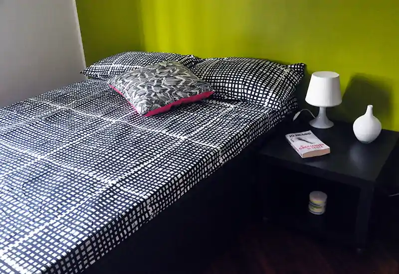 Bright, modern bedroom with patterned bedding, decorative cushions and a bedside table with lamp — clean, stylish and inviting for short-term rentals.