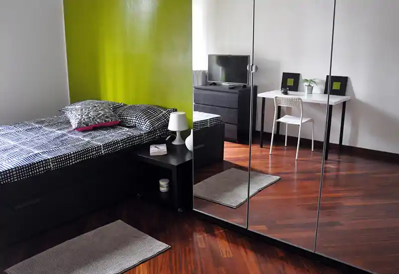 Bright, modern bedroom with a double bed, bedside table and large mirrored wardrobe that adds depth; simple desk by the window creates a functional workspace.