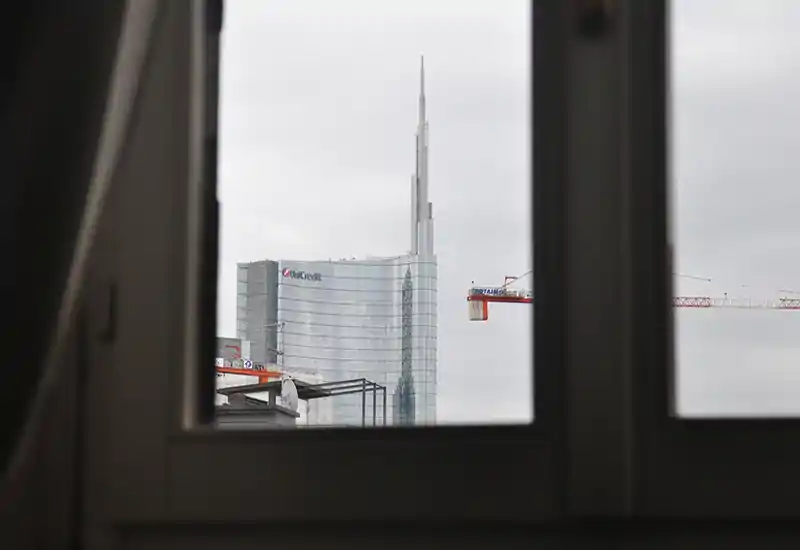 City view through a window framing a modern glass skyscraper and a construction crane on an overcast day.
