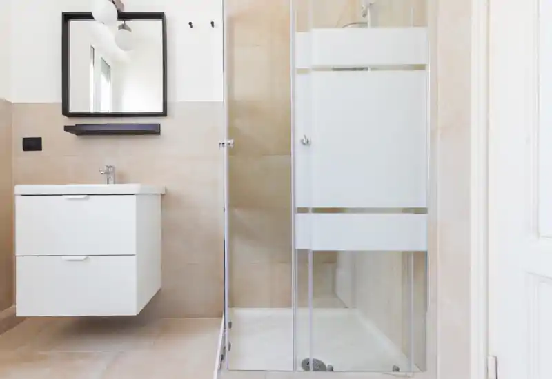 Bright, modern bathroom with a glass-enclosed shower, floating vanity and neutral beige tiles creating a clean, minimalist look.