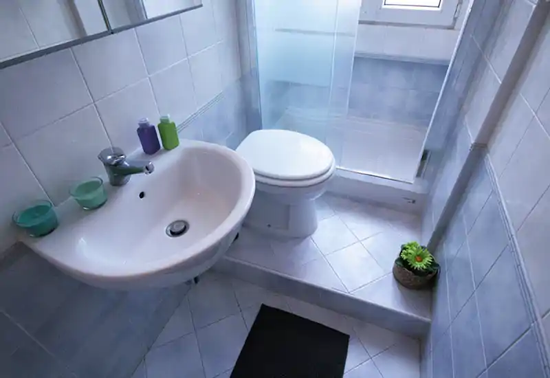 Compact, well-lit bathroom with a wall-mounted sink, toilet and a glass-enclosed shower; pale blue tiles and clean, modern fittings create a fresh look.