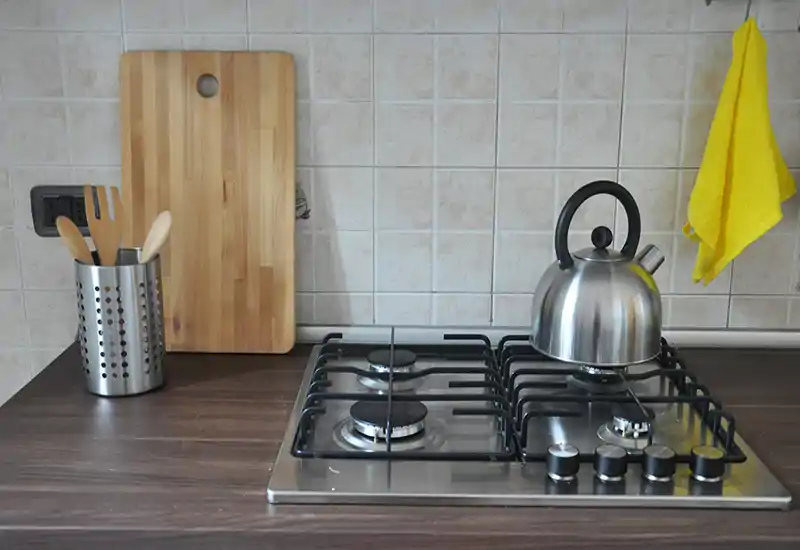 Well-styled kitchen counter with a gas cooktop, stainless-steel kettle, wooden cutting board and utensils — clean, bright and ready for cooking.