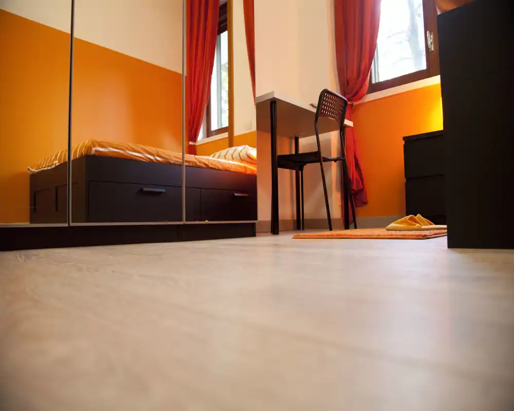 Camera da letto accogliente e ben curata con accenti arancioni, letto con cassetti contenitore, armadio con ante a specchio e una piccola scrivania vicino alla finestra.