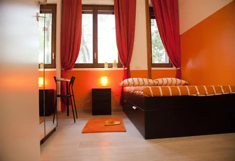 Camera da letto luminosa e accogliente con letto rialzato in legno scuro, biancheria a righe arancioni, tappeto coordinato e lampade sul comodino per un'atmosfera calda.