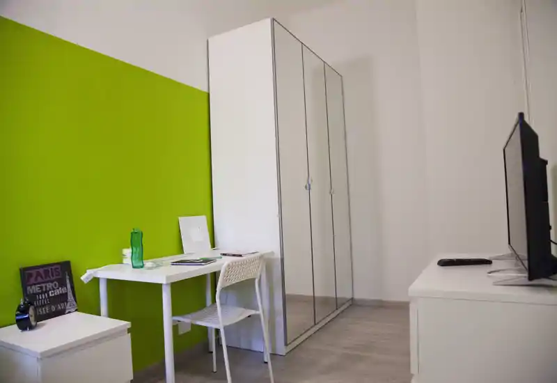 Compact bedroom corner with a white desk, mirrored wardrobe and bright green accent wall; clean, modern styling and good natural light.