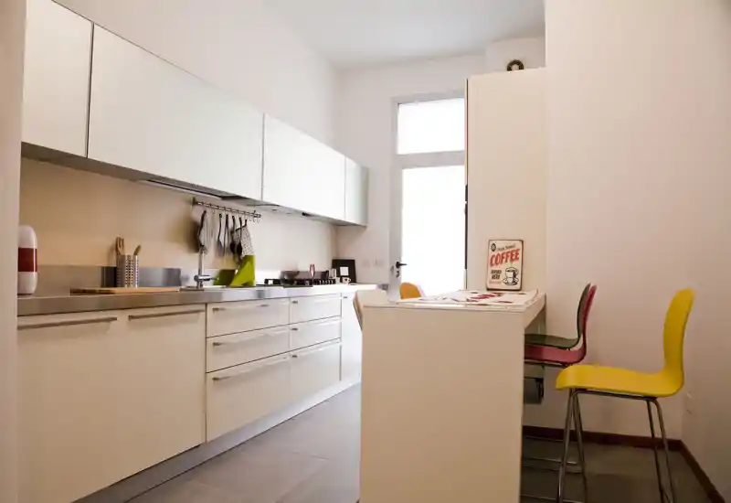 Bright, modern kitchen with white cabinetry, integrated appliances and a small breakfast counter with colorful stools — clean design and good natural light.