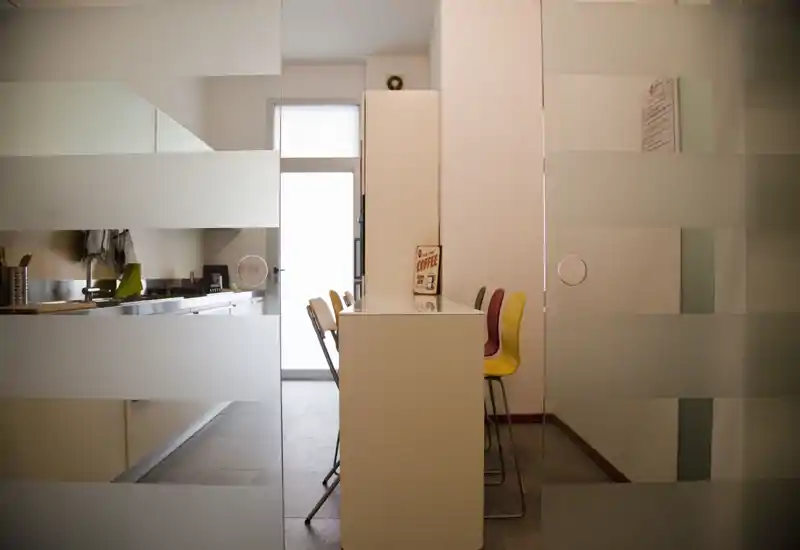 Compact modern kitchen with a breakfast counter and colorful bar stools. Frosted glass partition gives privacy while letting light through, and a bright back door provides natural illumination.