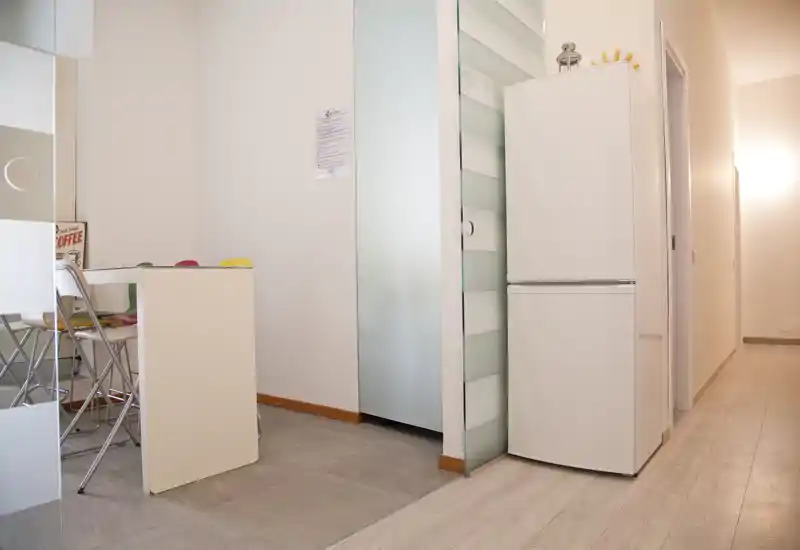 Compact kitchen area with a tall white refrigerator, small dining counter and colorful stools—bright, modern and space-efficient.