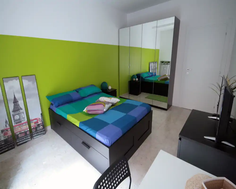 Camera da letto moderna e luminosa con ampio letto matrimoniale, biancheria dai colori vivaci e un armadio con ante a specchio che amplifica lo spazio.