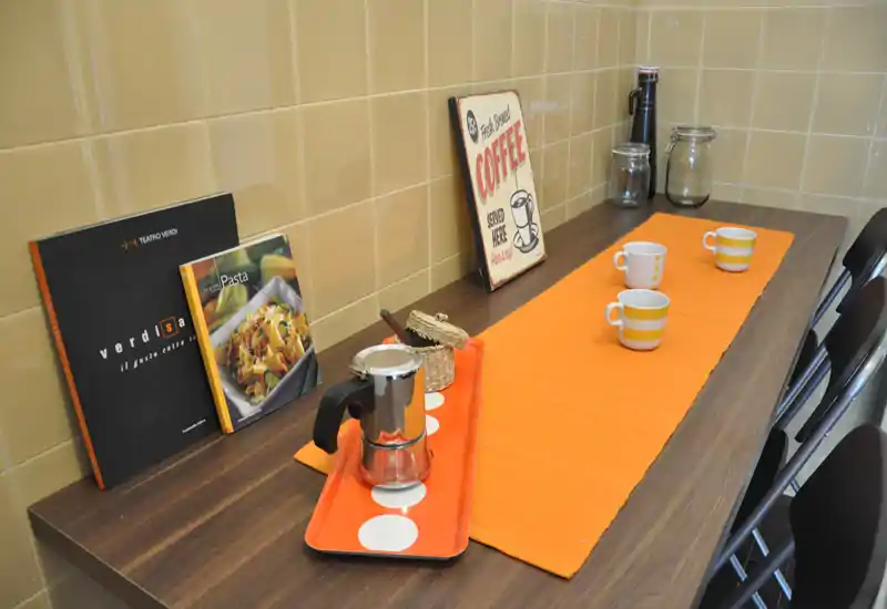 Bancone cucina luminoso e curato con runner arancione, caffettiera e tazze; ricettari e una targhetta "coffee" decorativa rendono l'ambiente accogliente.