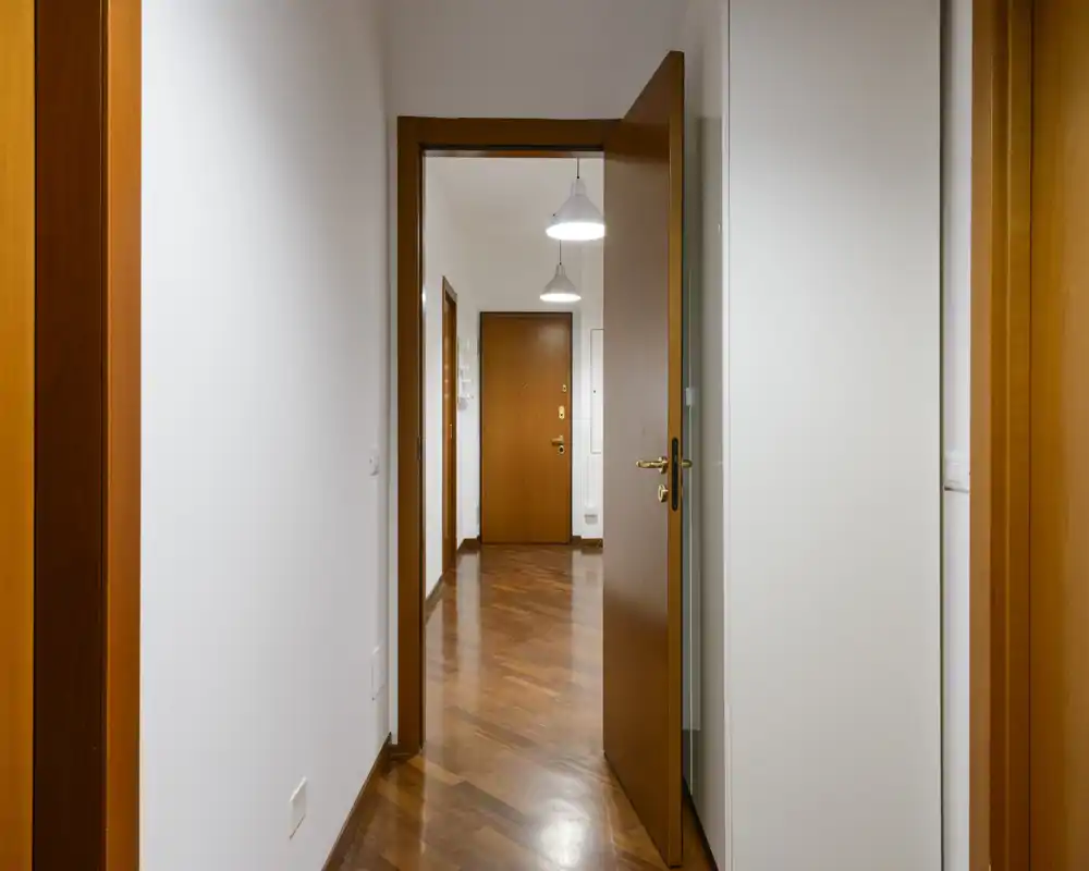 Bright, clean entrance hallway with wooden doors and polished parquet flooring, showing the apartment front door framed by warm wood trim.