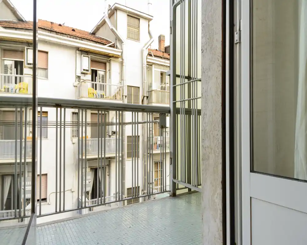 Small urban balcony with metal railing and tiled floor, looking toward neighboring apartment facades. Ideal for a morning coffee or drying clothes.