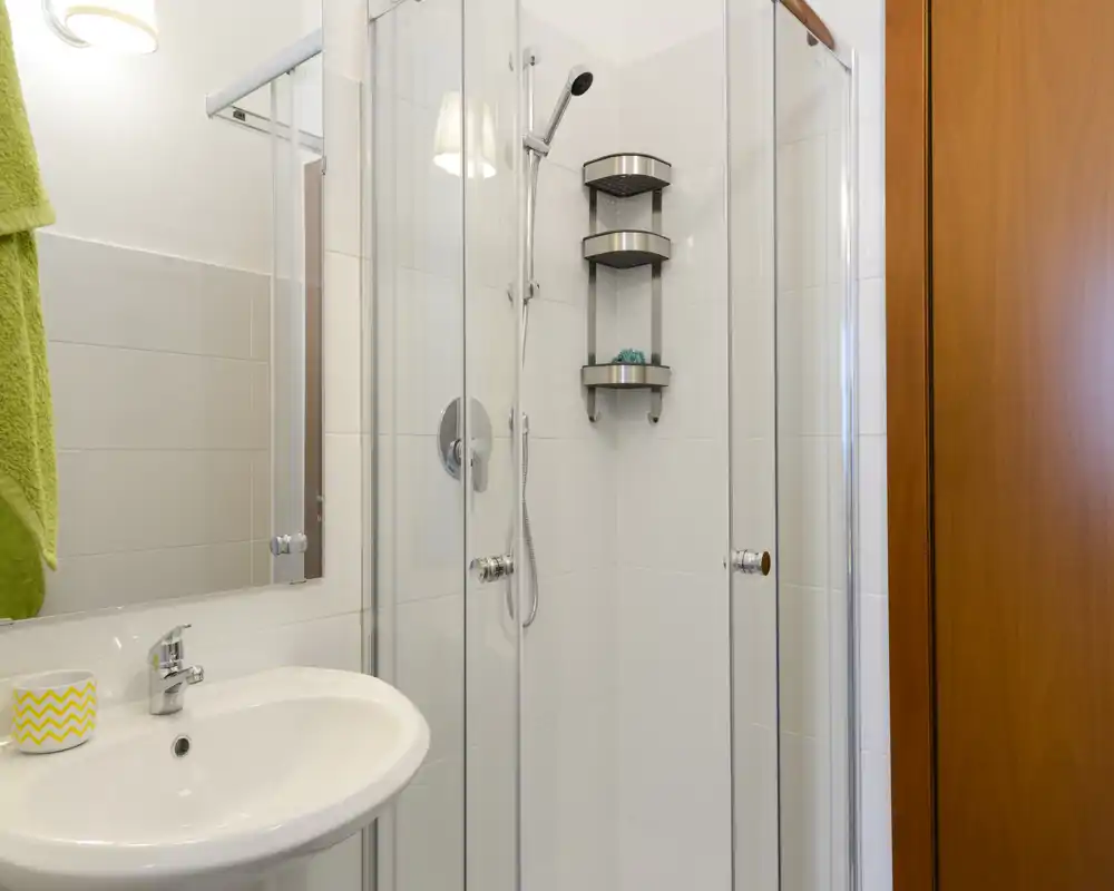 Bright, modern bathroom with a glass-enclosed shower, white tiles, a wall-mounted showerhead and a pedestal sink; clean and well-lit space ideal for rental photos.