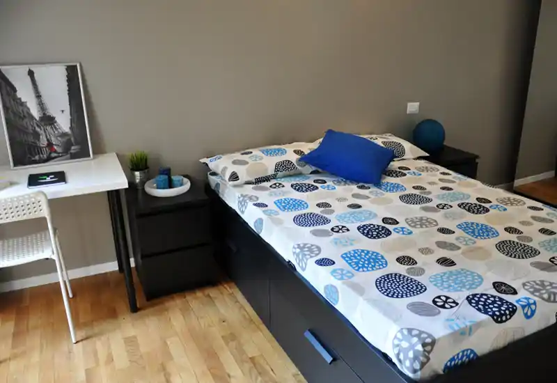 Bright, neatly styled bedroom with a double bed dressed in patterned linens, a blue accent pillow and matching bedside tables — ideal for rental listings showcasing a clean, modern sleeping area.