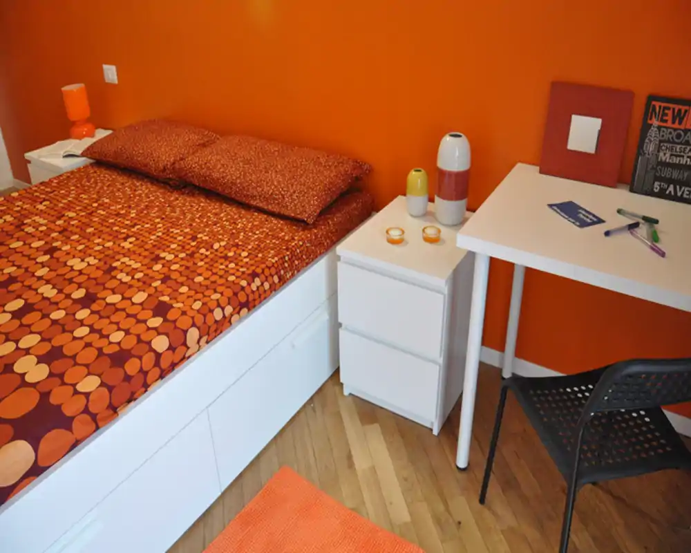Camera da letto compatta e stilosa con toni arancioni coordinati, letto ampio con biancheria a fantasia, comodini bianchi e un piccolo spazio lavoro — luminosa e accogliente per soggiorni brevi.