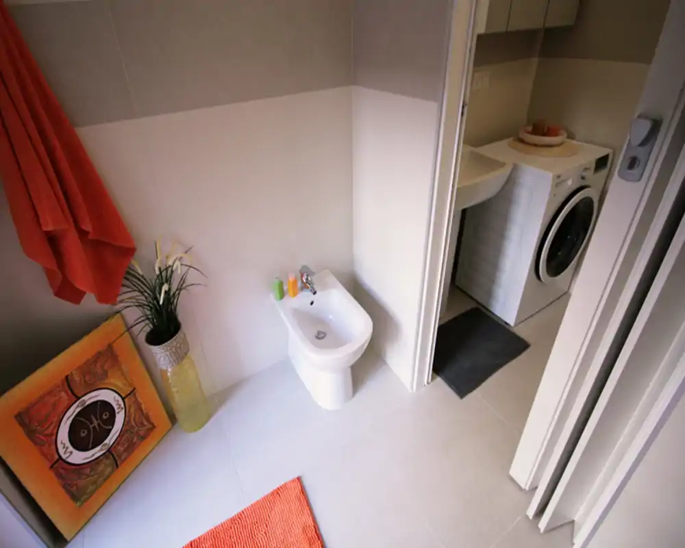 Baño moderno y limpio con bidé, toallas decorativas, alfombra y una vista parcial de la zona de lavandería con lavadora.