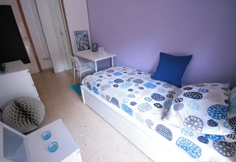 Single bedroom with a neatly made bed, blue-and-white patterned bedding and a small desk by the wall; fresh, tidy and well lit — ideal for a student or single occupant.