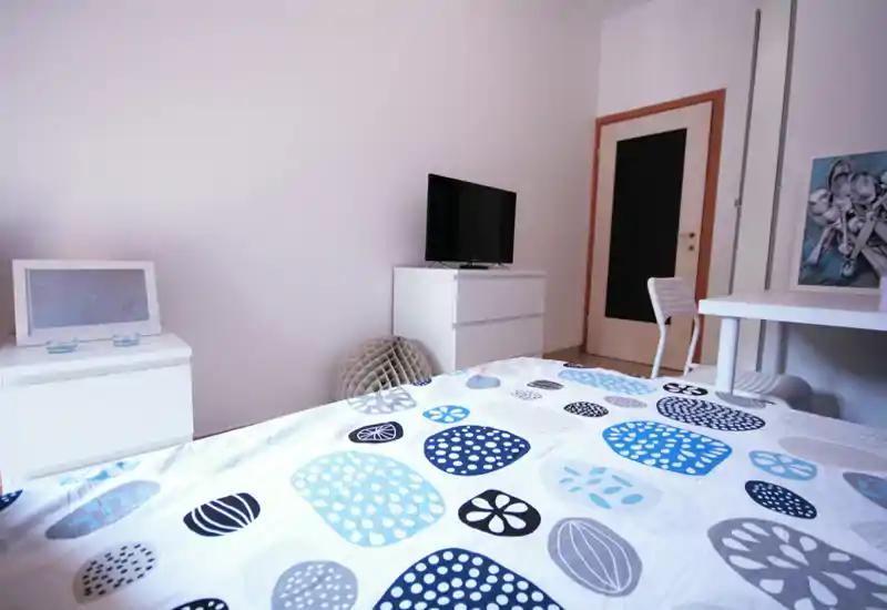 Chambre moderne et lumineuse avec une couette à motifs, télévision sur une commode et un petit coin bureau — confortable et bien éclairée.