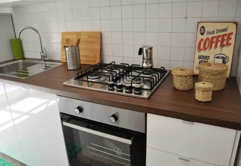 Bright, modern kitchen counter with a gas cooktop, built-in oven and stainless sink; styled with a cutting board, utensil holder and wicker baskets for a cozy, lived-in look.