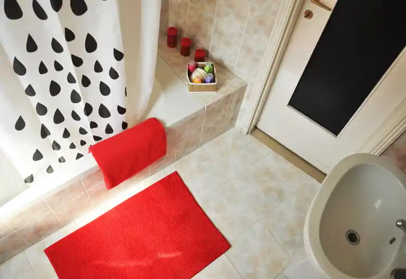 Bright, tidy bathroom with a bathtub (shower curtain), white sink and red bath mat and towel creating a bold accent.