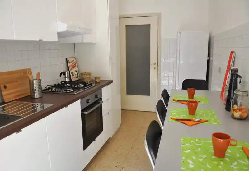 Bright, tidy kitchen with white cabinets, built-in oven and a breakfast bar set with green placemats and orange cups — practical and welcoming space.