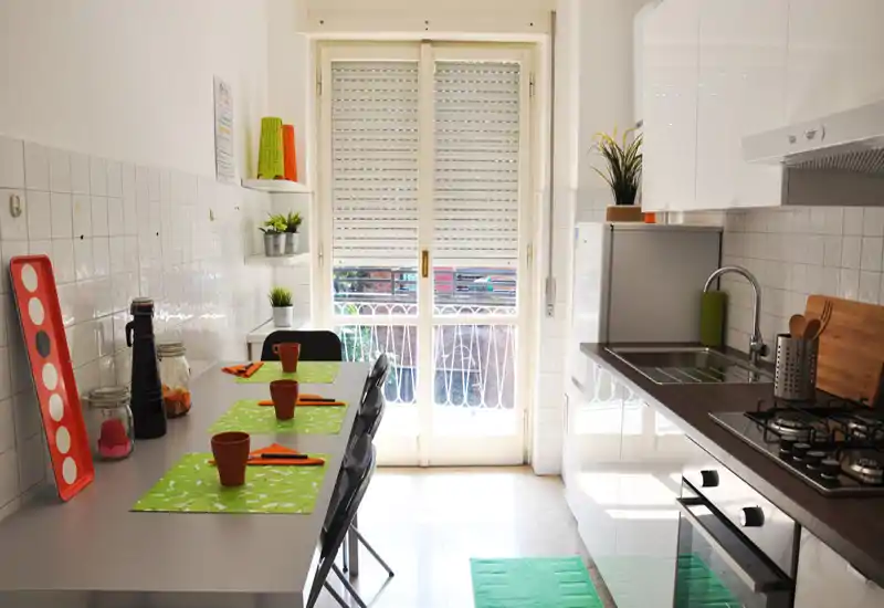 Bright, modern kitchen with a full countertop, gas hob, sink and a casual dining table set for four beside a glass door leading to a small balcony.