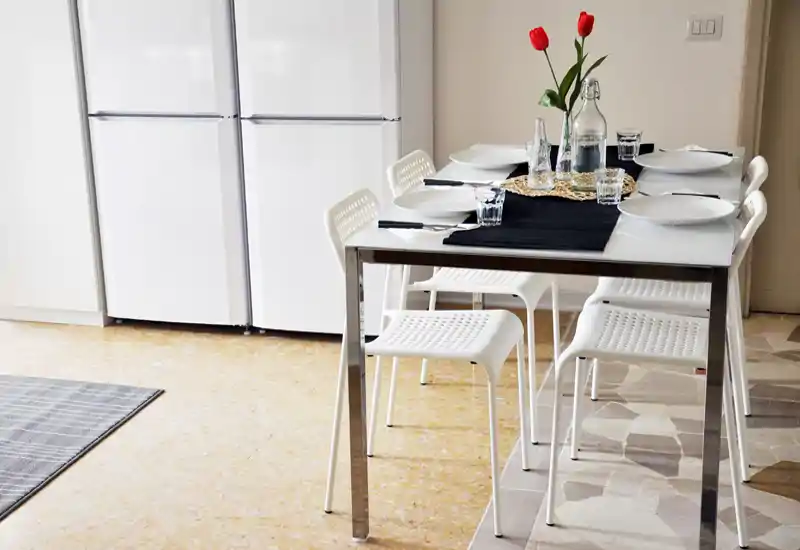 Bright, modern dining area with a glass-top table set for six, white perforated chairs and a simple floral centerpiece.