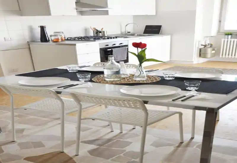 Modern, bright kitchen with a gas stove and a set dining table for four — clean white cabinetry, natural light and simple contemporary decor.