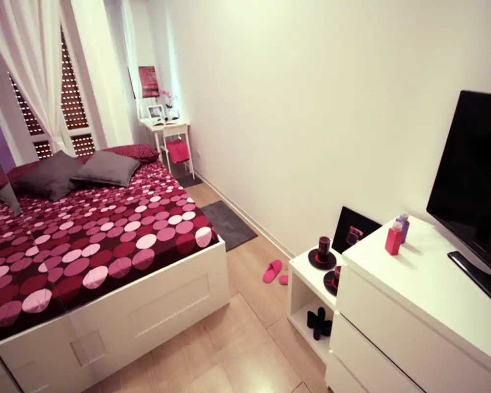Bright, cozy bedroom with patterned duvet, bedside table and a dresser with TV — well-styled small double room ideal for a comfortable stay.