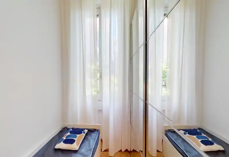 Small bright entrance or vestibule with a bench and mirrored wardrobe, soft sheers on the window that filter light and add privacy.