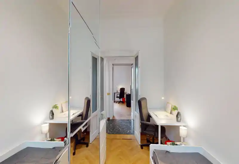 Compact bedroom with a single bed and a workspace: narrow room featuring a small bed, two desks with office chairs and bright white walls that create a clean, functional atmosphere.