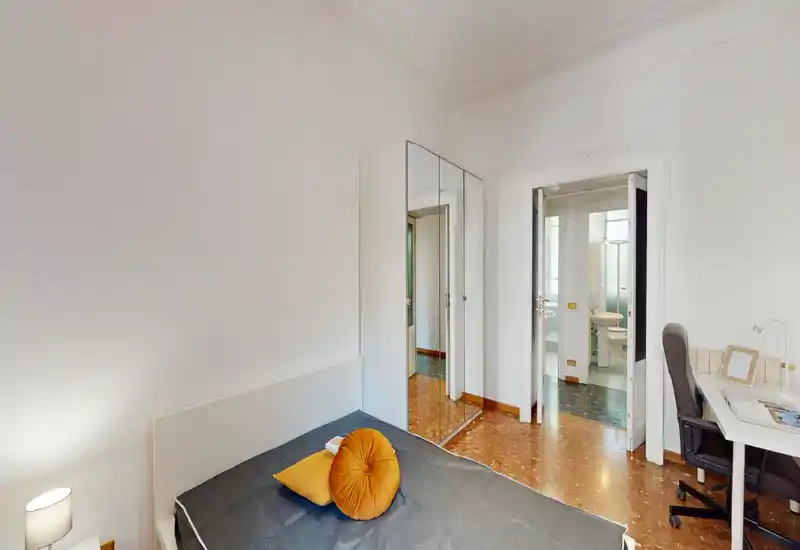 Compact bedroom with a single bed, decorative round cushion and bedside lamp; mirrored wardrobe and a small desk make the room functional and bright.