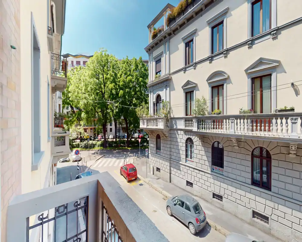Sunny balcony view overlooking a tree-lined street and classic city façades, with space for small outdoor seating.