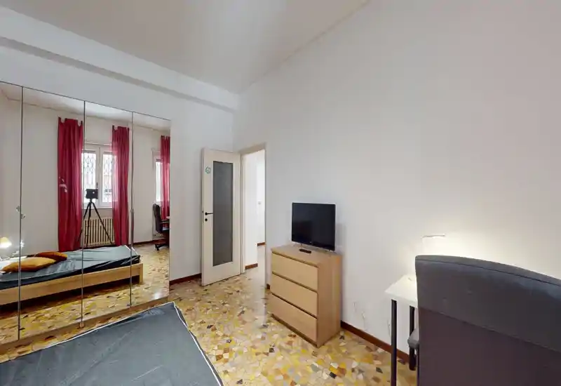 Dormitorio luminoso y de mobiliario sencillo con cama doble, armario con espejo y una pequeña zona de escritorio. La luz natural y el suelo cálido hacen la estancia acogedora.