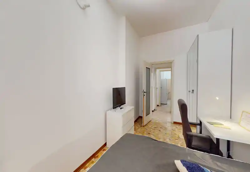 Dormitorio compacto con cama individual, armario, escritorio y silla. Espacio luminoso y decorado de forma sencilla, ideal para estudiante o persona sola.